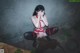 A woman in a red and black lingerie sitting on the ground.