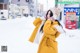 A woman in a yellow coat is standing in the snow.