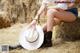 A woman sitting on a pile of hay with a cowboy hat.