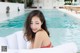 A woman in a red bikini sitting on an inflatable mattress by a pool.