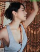 A woman in a gray tank top standing in front of a wall of beads.