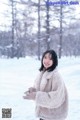 A woman standing in the snow wearing a coat and gloves.